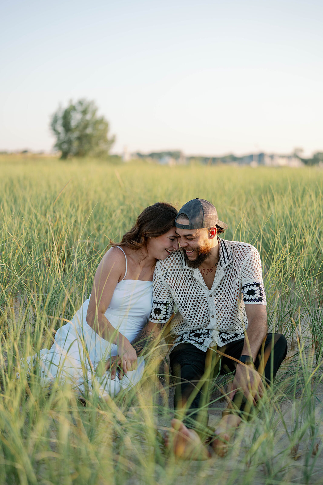Engaged couple sitting in tall dune grass during dreamy Lake Michigan sunset engagement session