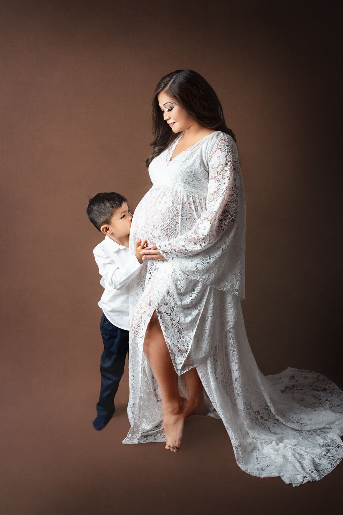 expecting mother in long white lace gown posing with her older son