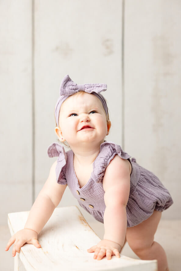 One year old girl in purple scrunches her nose for her photos.