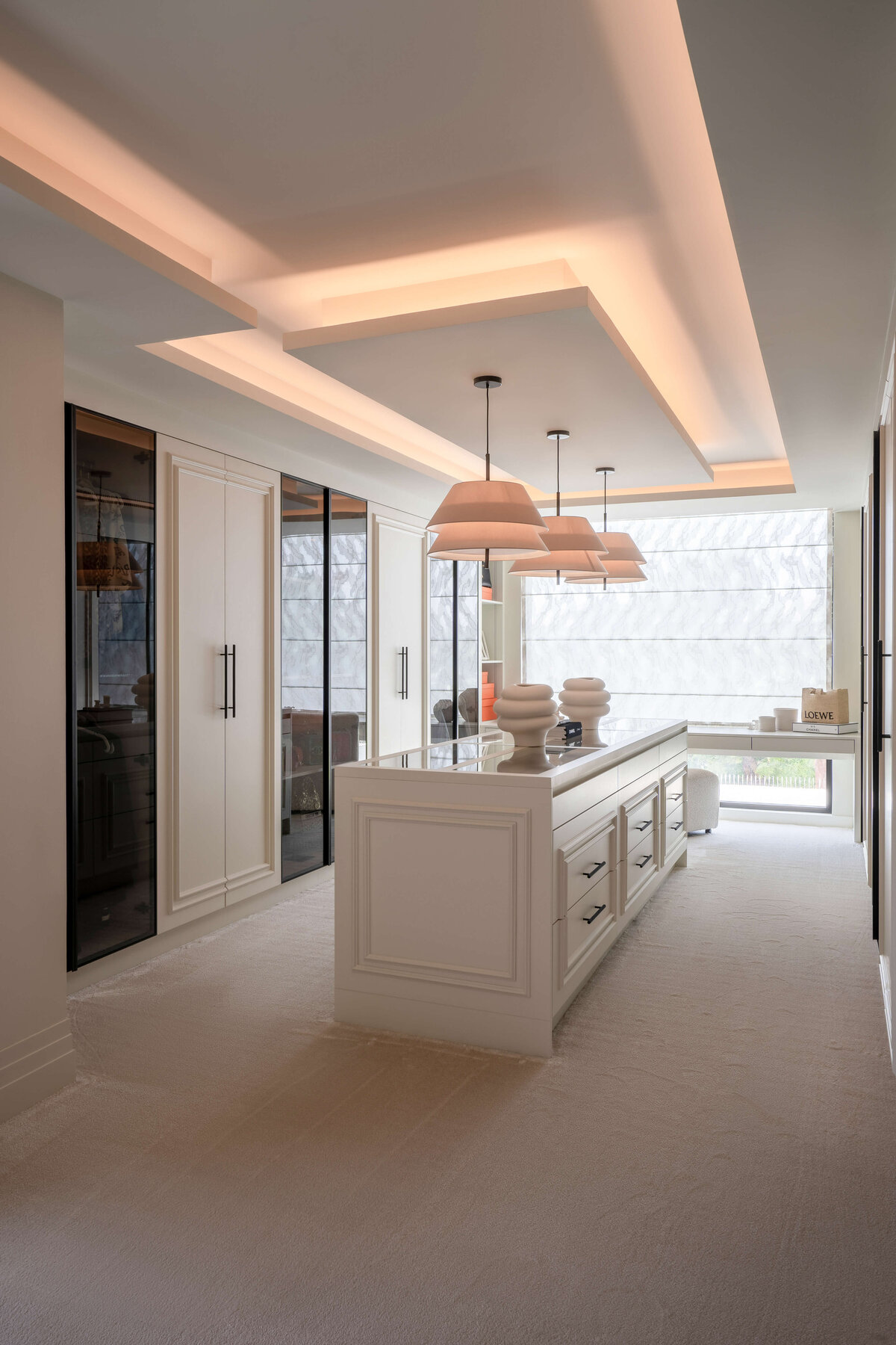 Spacious primary dressing room with built-in closets lining walls to the left and right, with a large closet island with storage in the center.