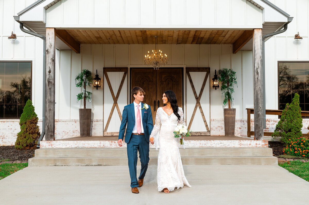 Newlyweds holding hands walking outside of white barn in Murfreesboro, TN