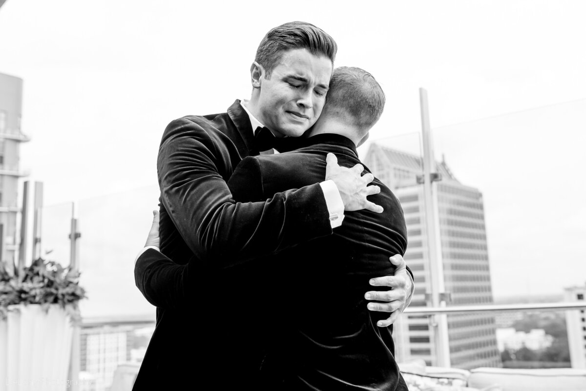 Emotional same-sex wedding first look at Merchant and Trade rooftop in Uptown Charlotte, NC with two grooms embracing before their ceremony.