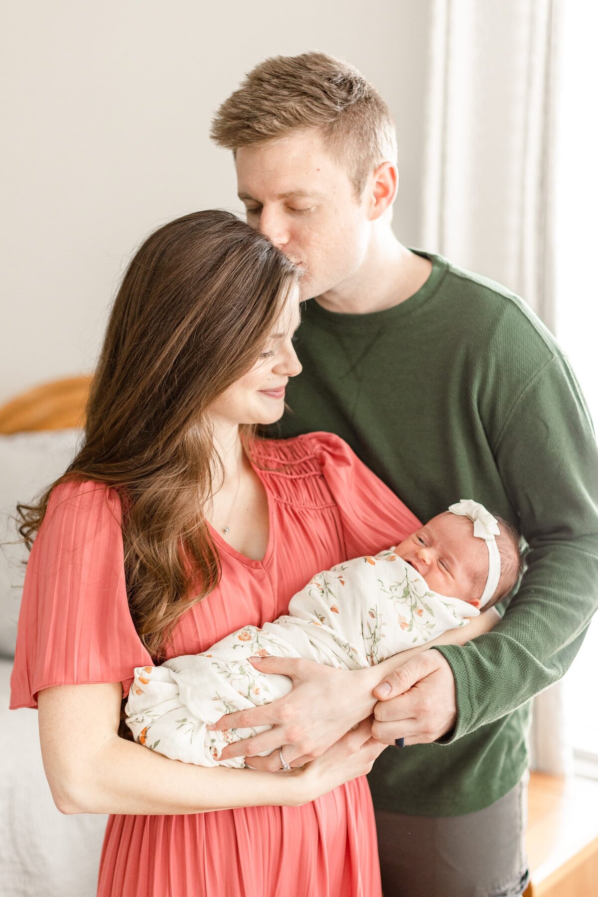 a man kissing his wife on the head while she holds their baby