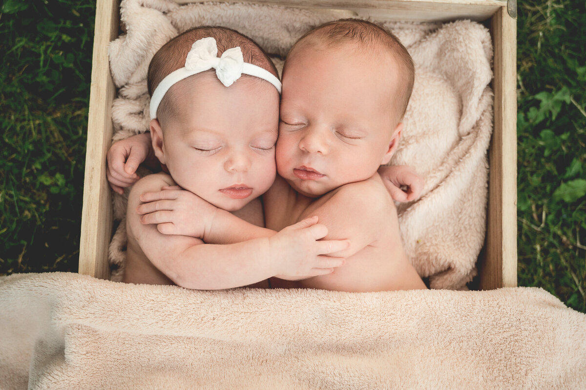 Newborn girl and boy twins sleeping with arms wrapped around each other hugging at their outdoor photo session.