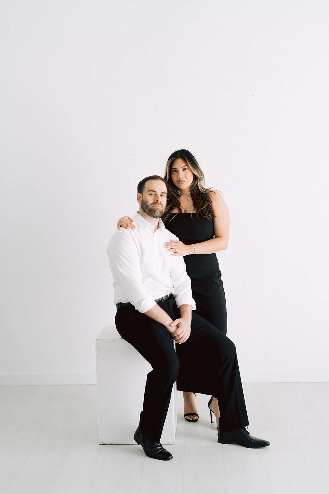 A couple in formal black and white attire pose together against a white wall at the Lumen Room