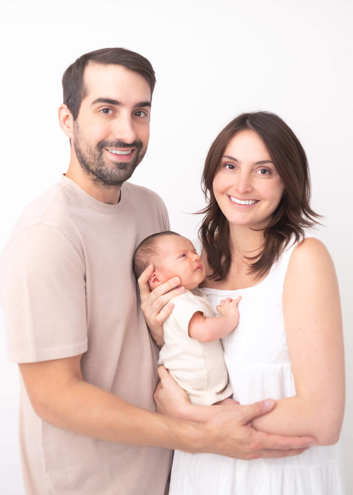 Beautiful new family in studio portrait with white backdrop wearing white and beige
