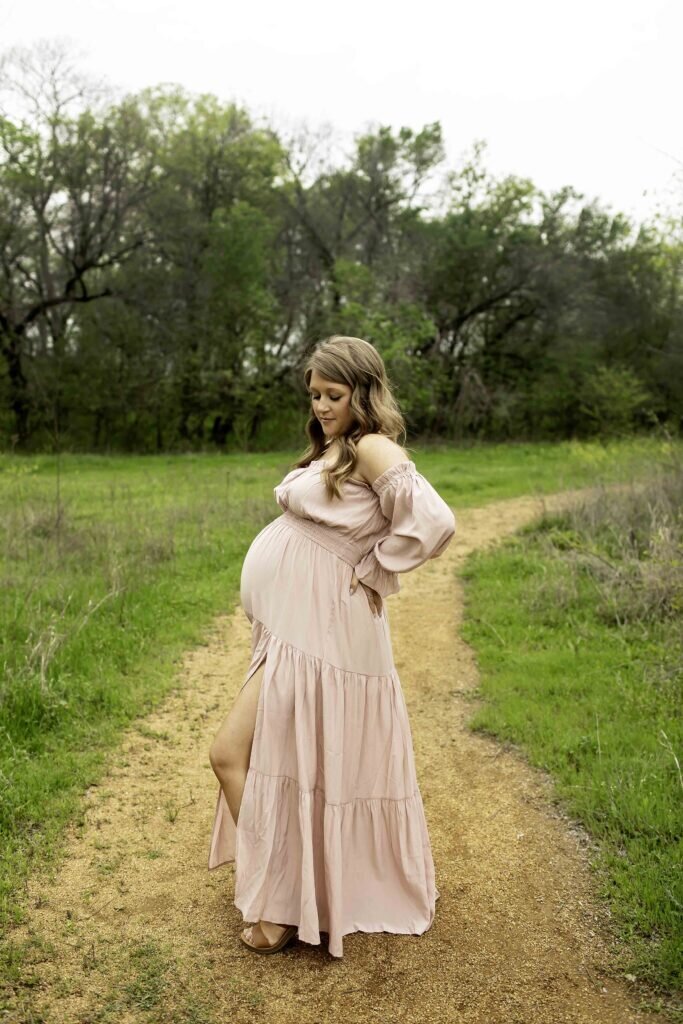 A beautiful maternity photo of the expectant mom in a soft, flowy pink dress, standing elegantly with her hands lovingly placed on her belly, surrounded by soft, dreamy lighting, captured by Chunky Monkey Photography.