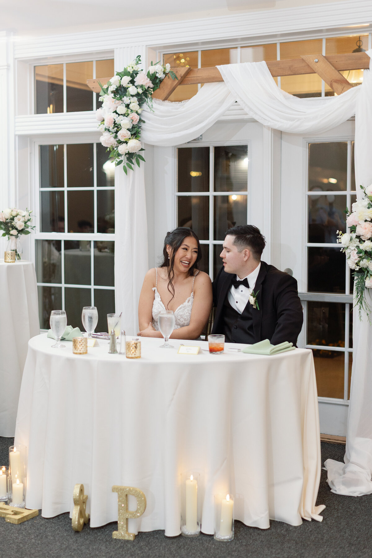 Bride and groom at sweetheart table decorated with candles, florals, and gold initials during Springfield Manor reception.