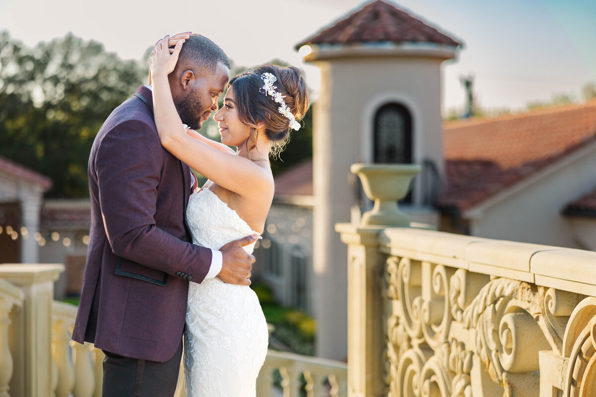 Witness the love and warmth of a wedding day with this enchanting photo of a bride and groom embracing on their venue's balcony at sunset, capturing a moment of pure romance.