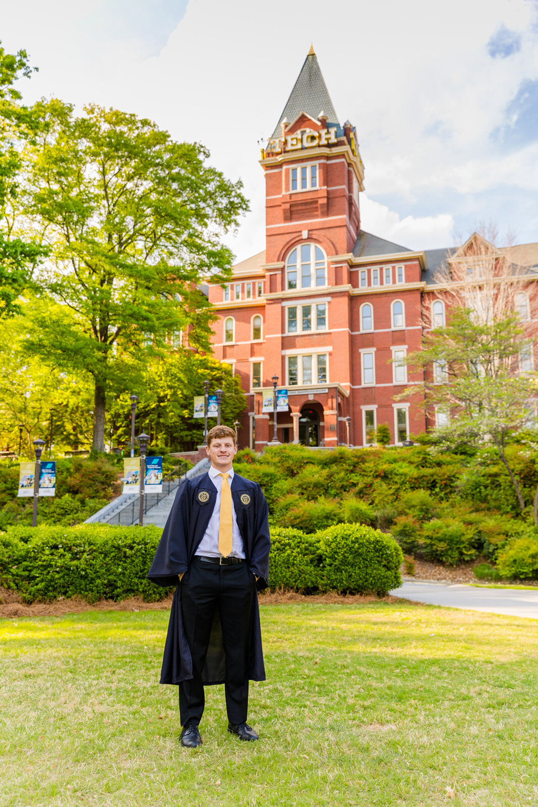 GT senior boy standing on graduation outfits cap and gown on the campus lawn in front of the Georgia tech tower during portraits by Atlanta photographer Laure Photography