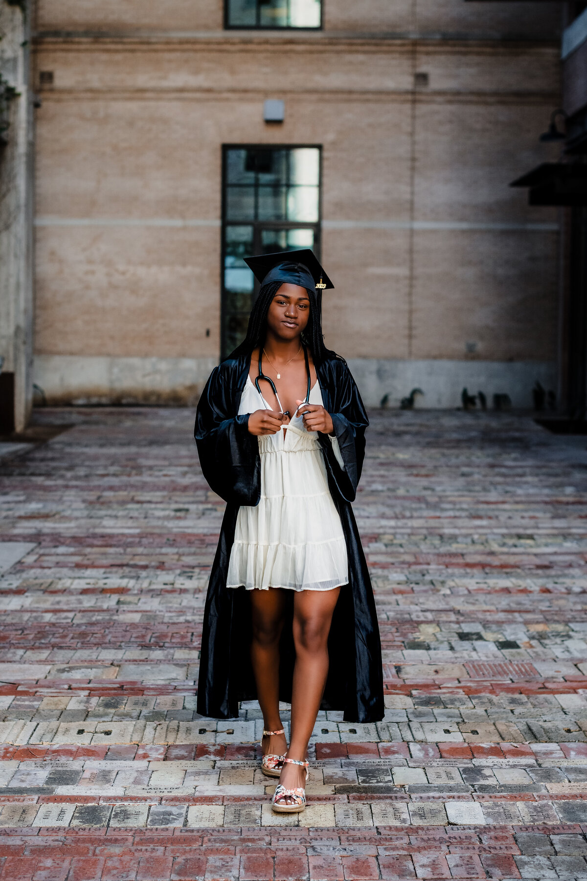Close-up of senior girl smiling while walking  holding stethoscope in graduation gown at The Pearl.
