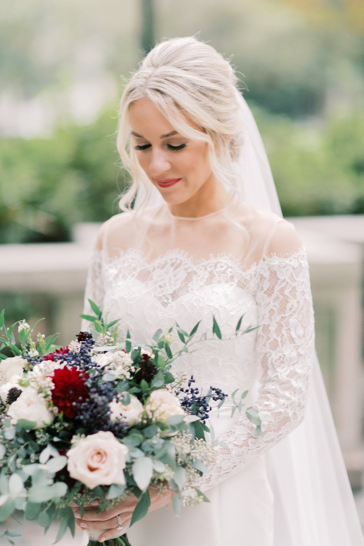 bride looking down at bridal bouquet wearing long lace veil