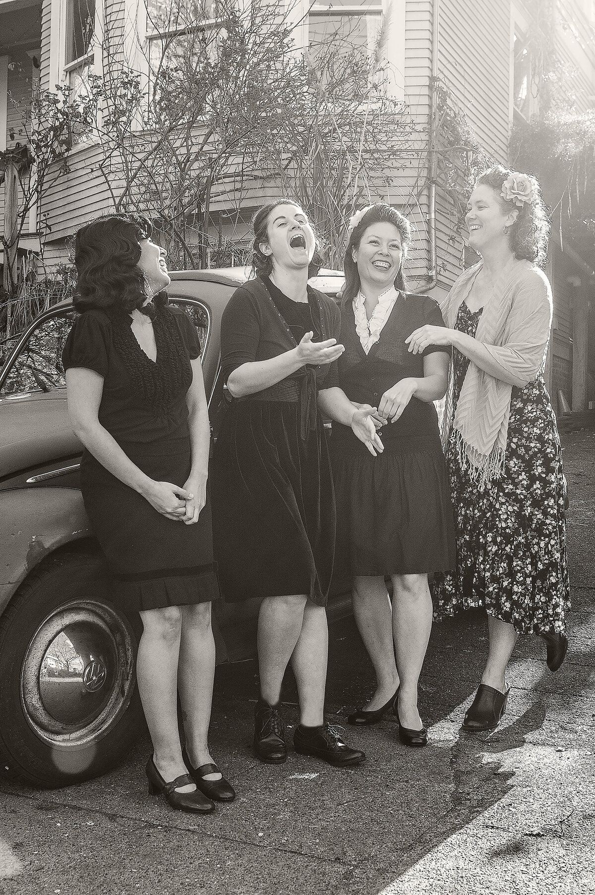A group of women laughing while standing next to a vintage car