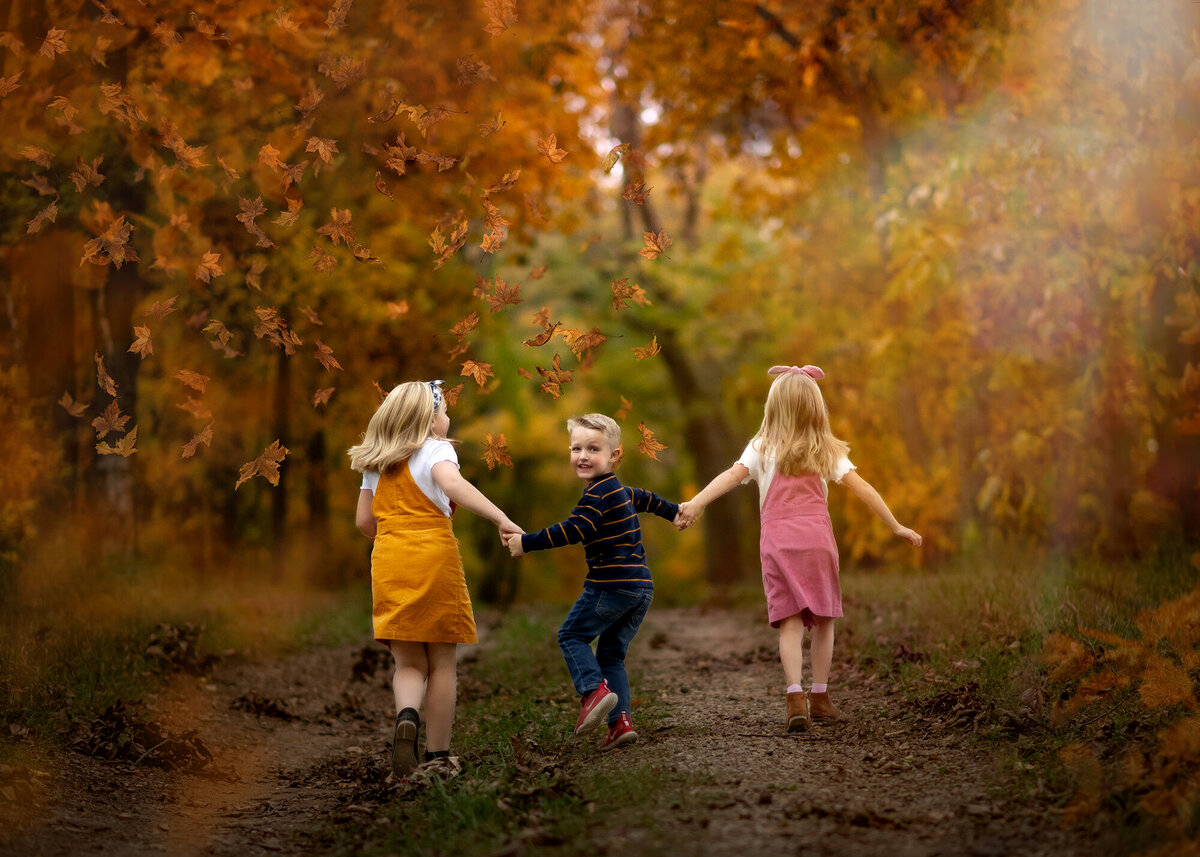 3 kids run down a path surrounded by fall leaves
