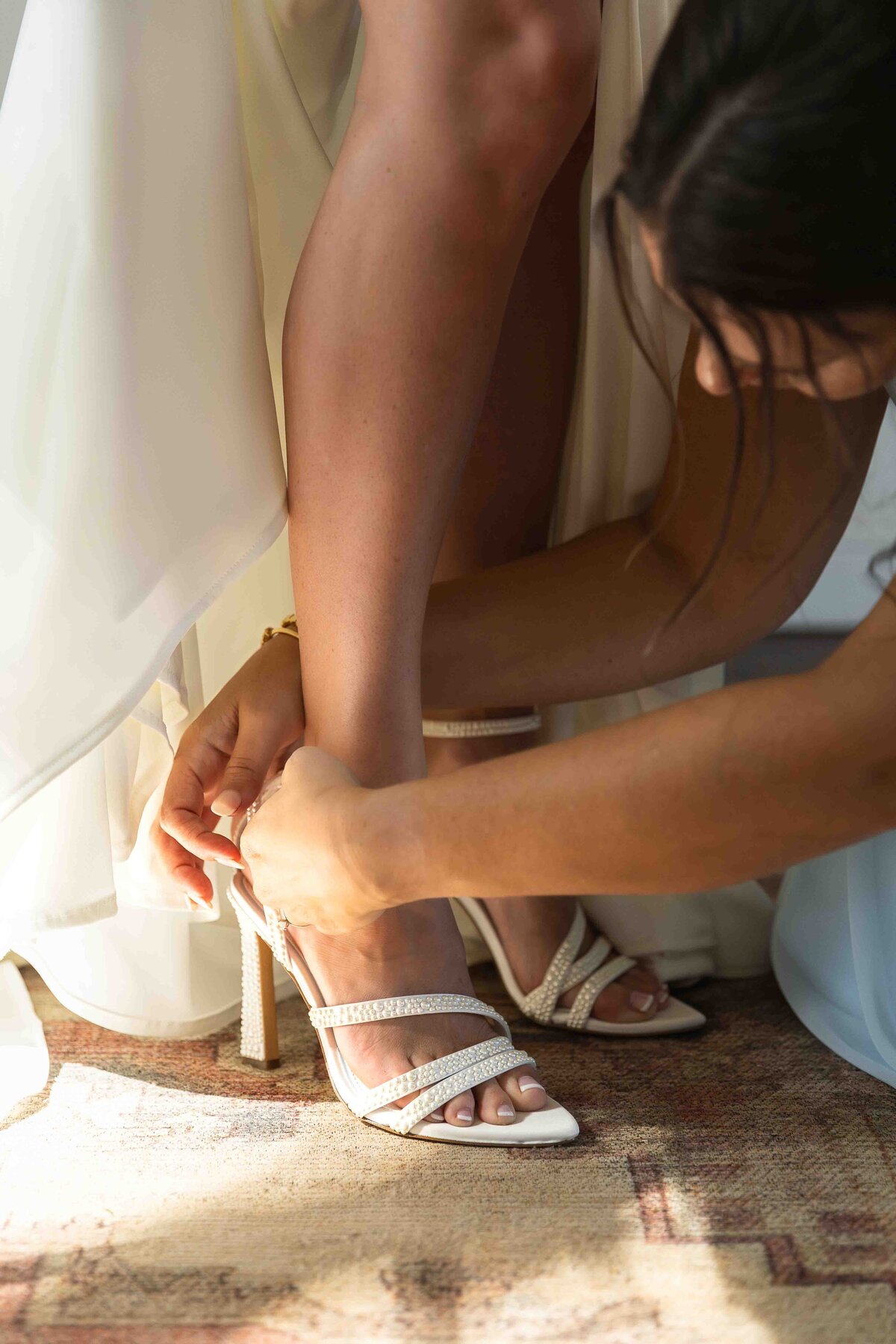Bridesmaid helping bride put her bridal shoes on