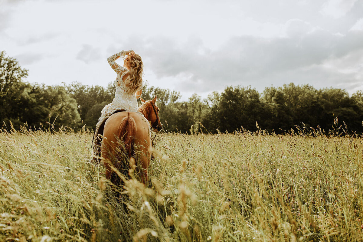 Bride on horseback in a field, looking out towards the horizon