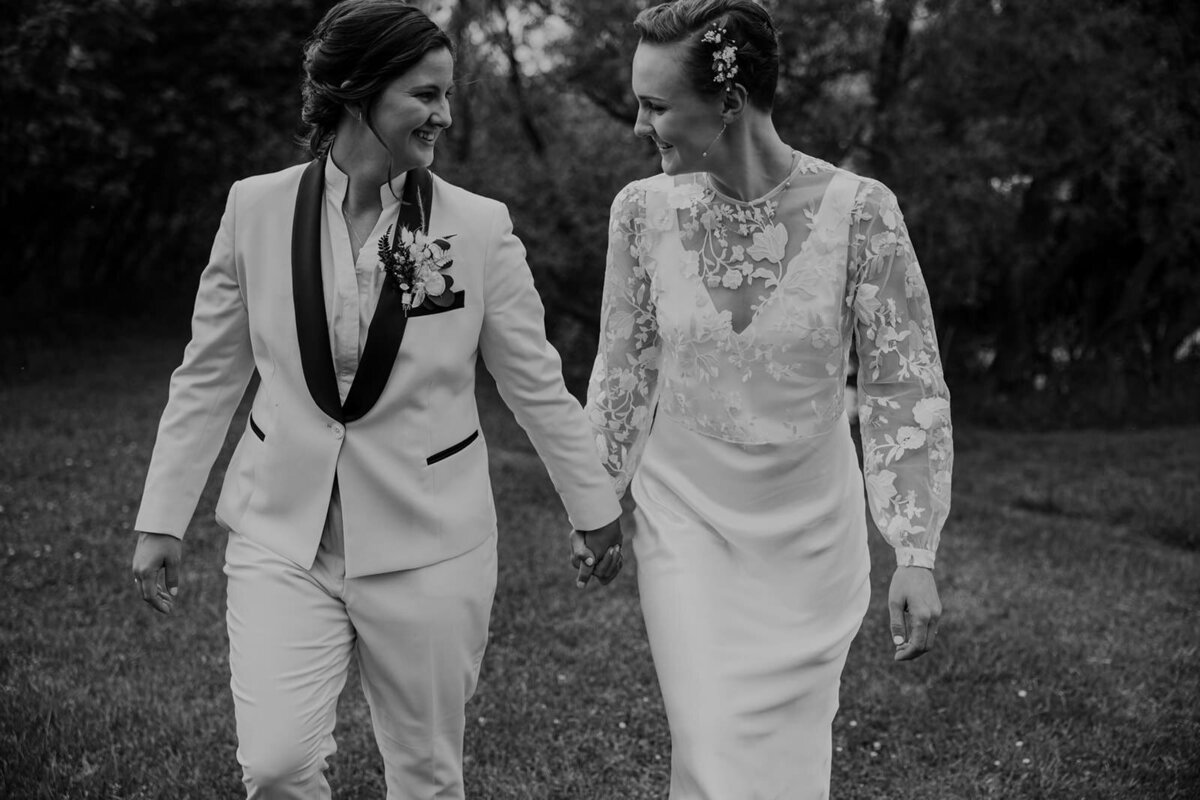 Two brides are walking holding hands and smiling on their wedding day