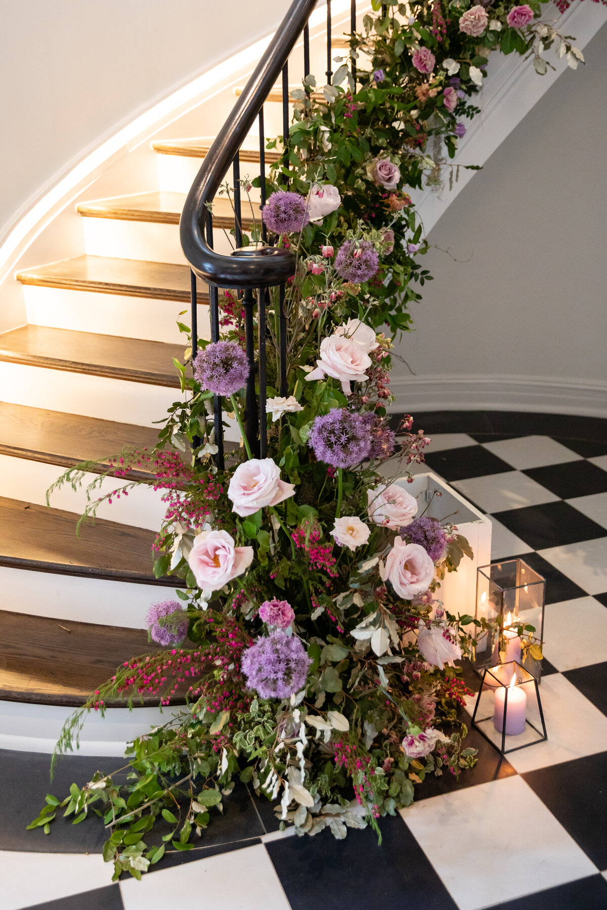 Lush floral installation growing up the staircase with natural greenery, purple globe allium, blush garden roses, and pastel wildflowers. Bridgerton inspired engagement party at a private home in Nashville, TN.