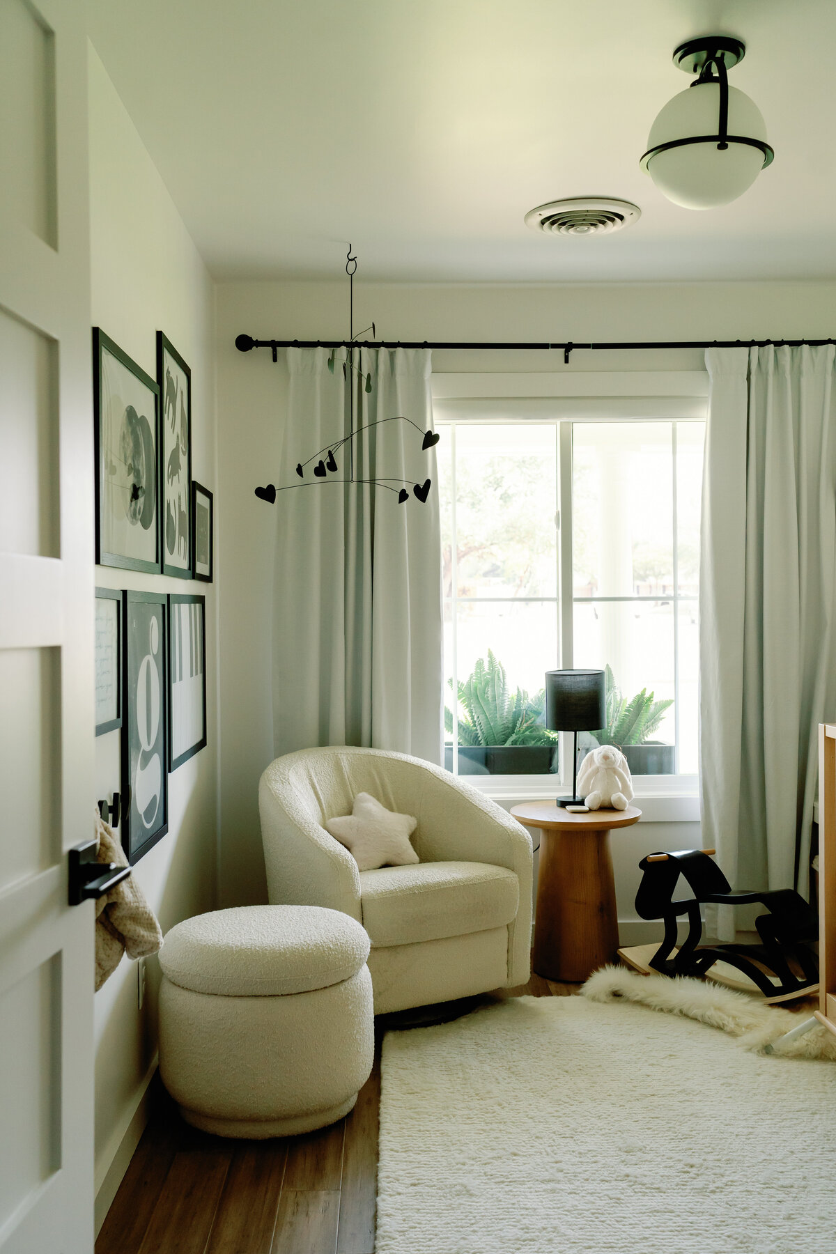 white boucle chair in nursery with black mobile, gallery wall and white rug