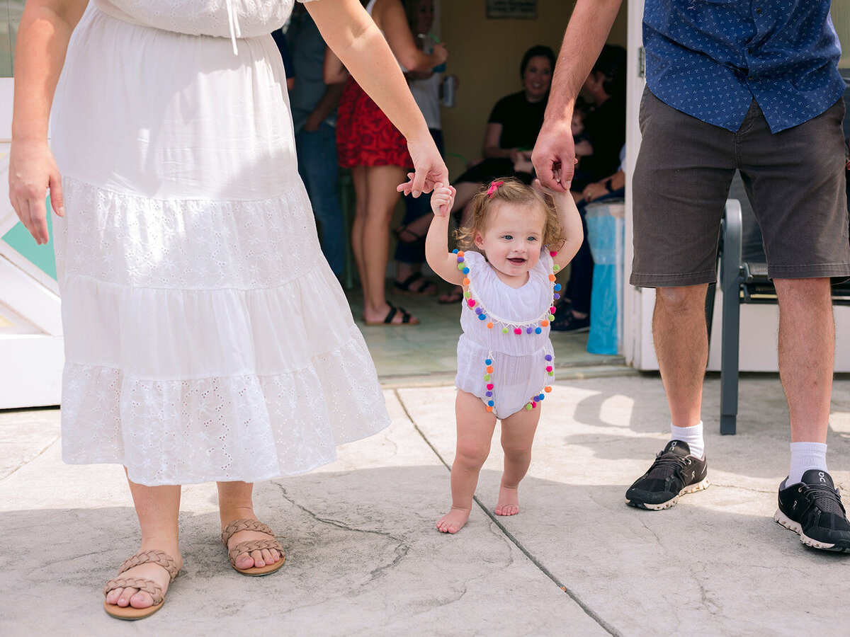 Mom and dad holding their baby as the little one walks around during a first birthday party in a Bay Area backyard.