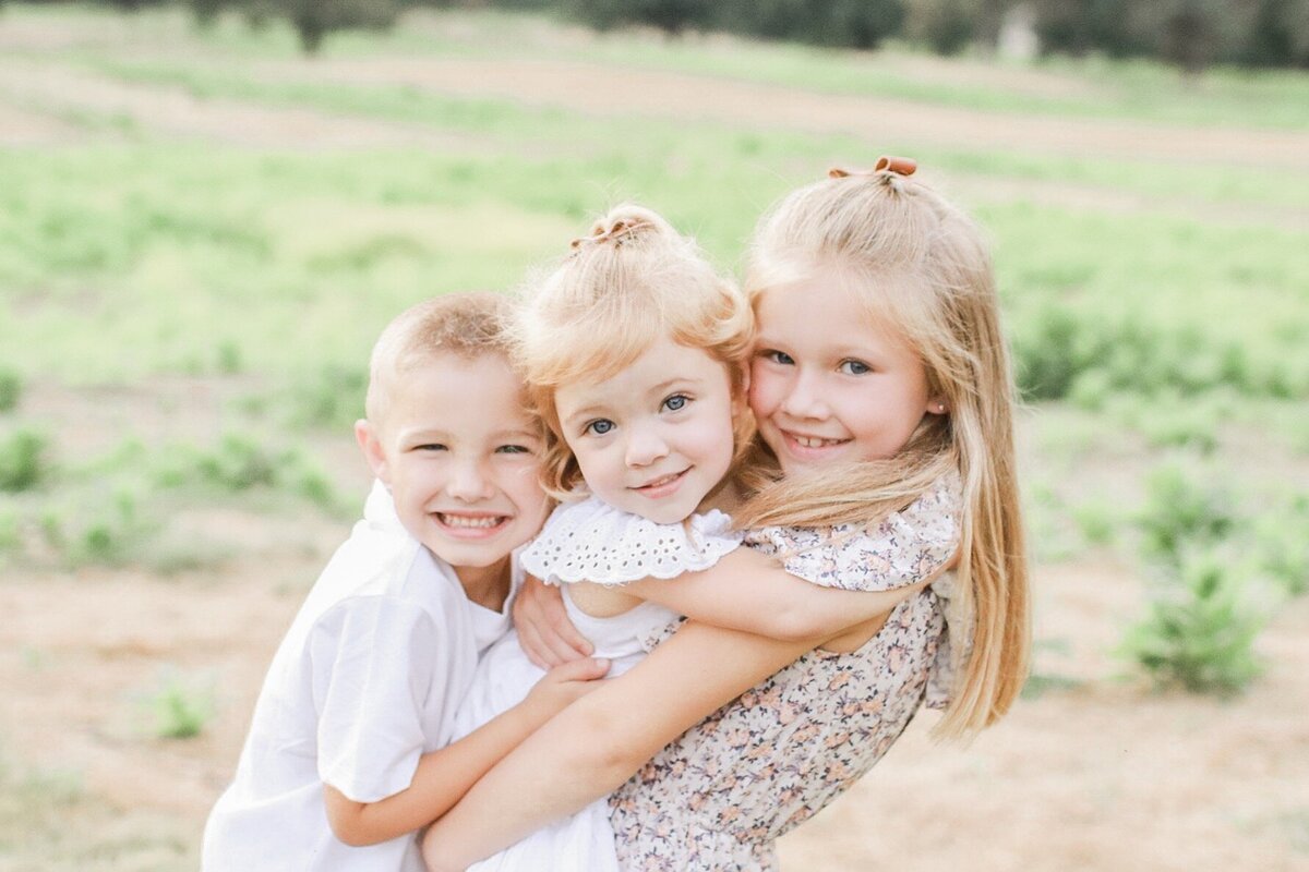 three siblings hugging each other and smiling