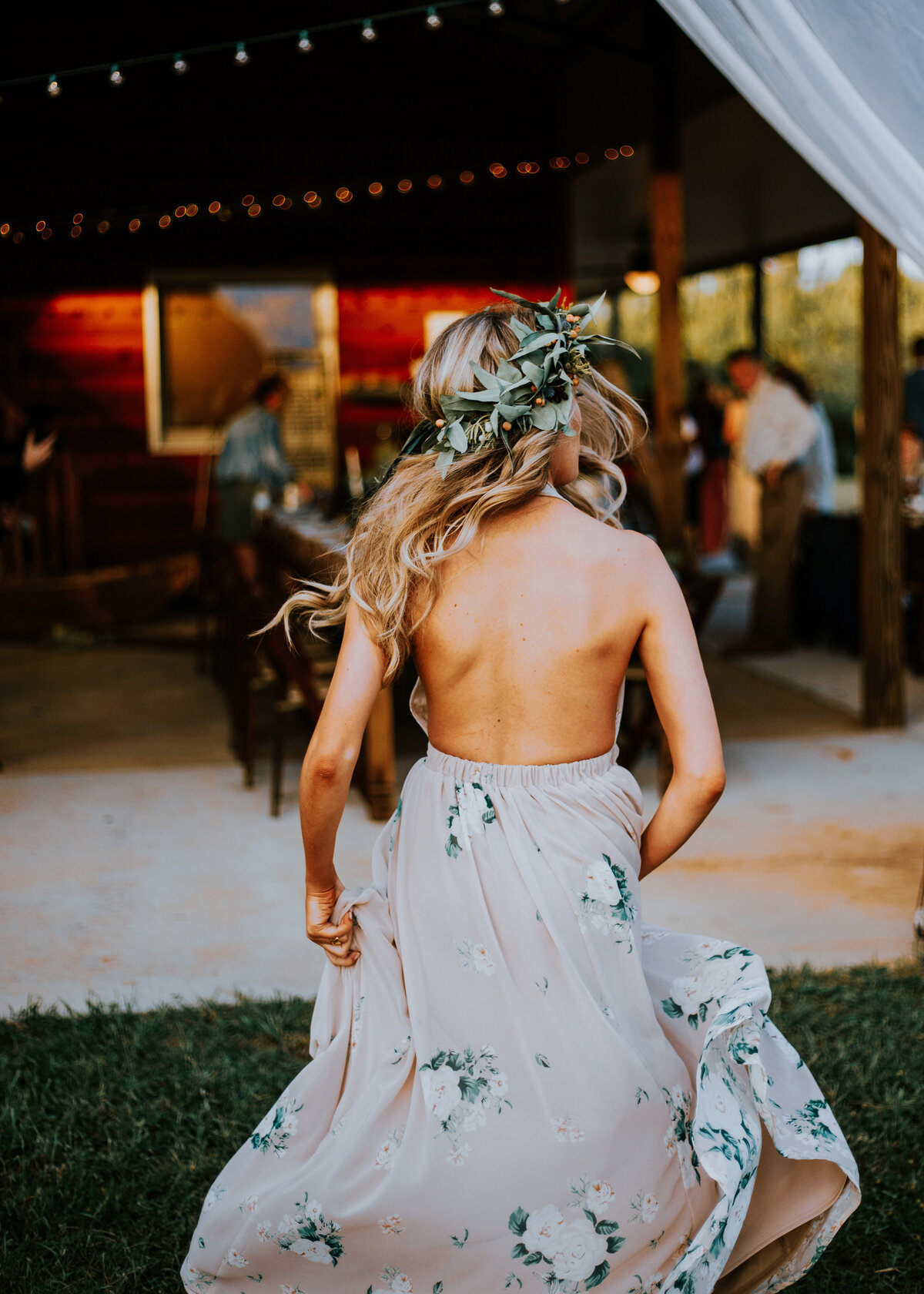 A boho bridesmaid runs towards a rustic country wedding with a green floral headband crown.