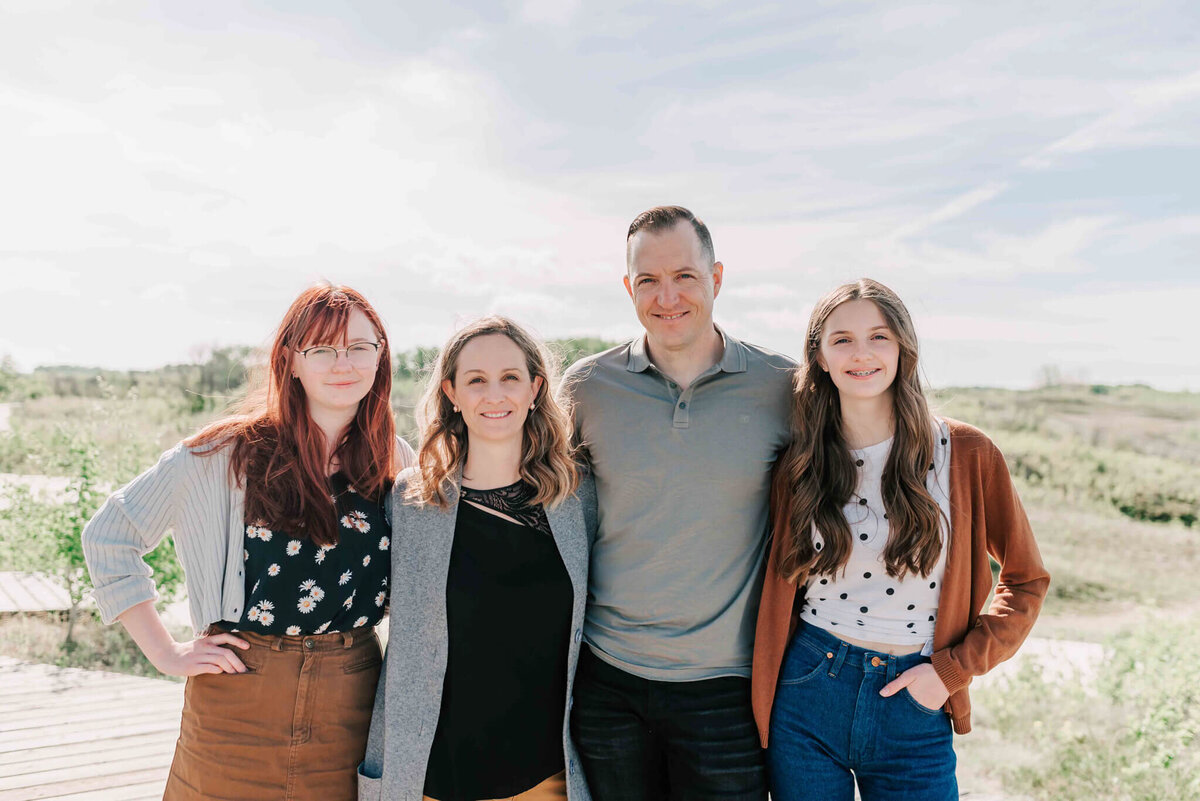 Close up of a family of 4 standing on a bare patch of grass on a hill side. 