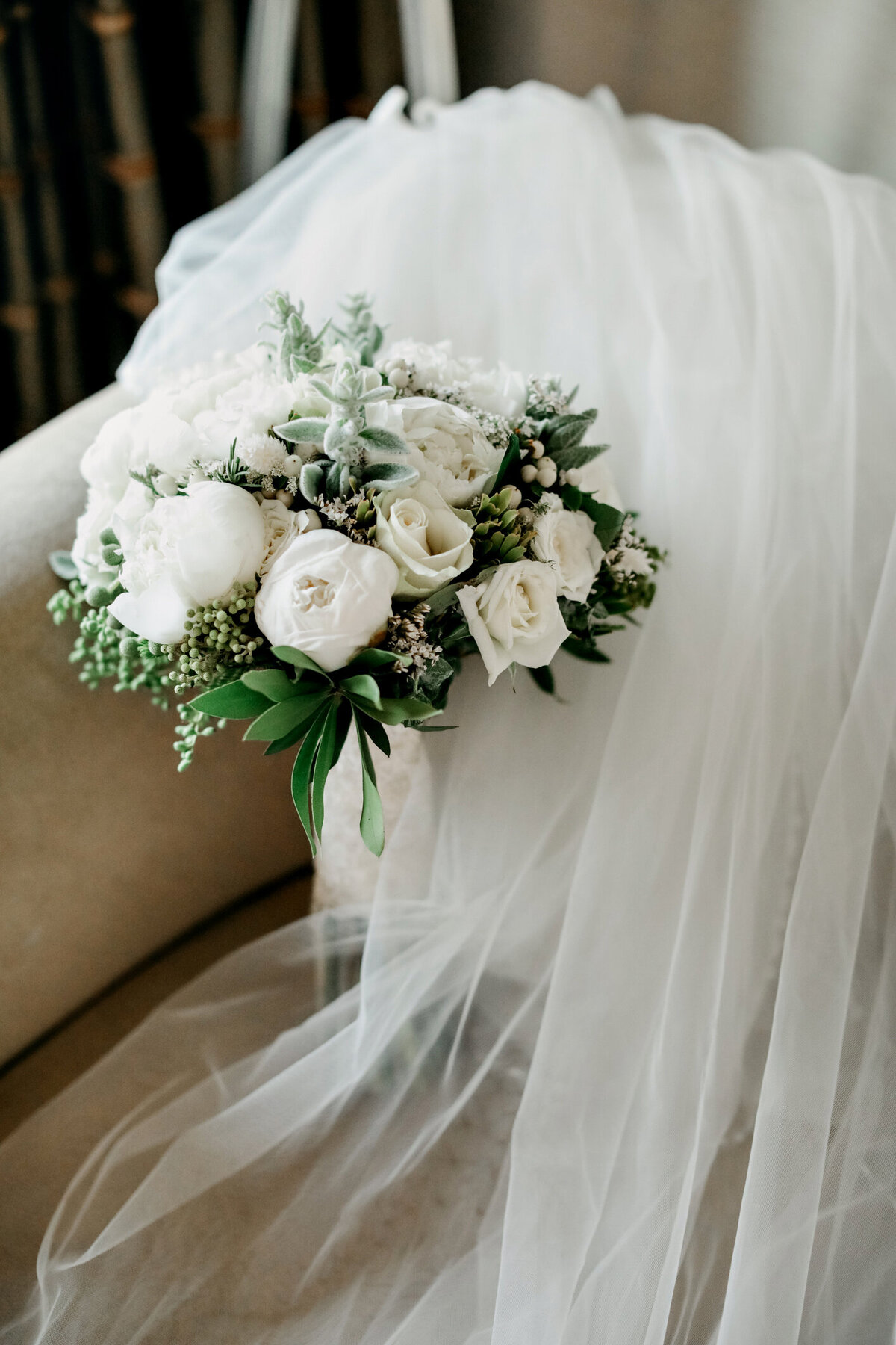 Elegant white floral bouquet featuring roses and peonies, beautifully displayed against the soft fabric of a wedding gown, designed by In Full Bloom Event Planning & Design