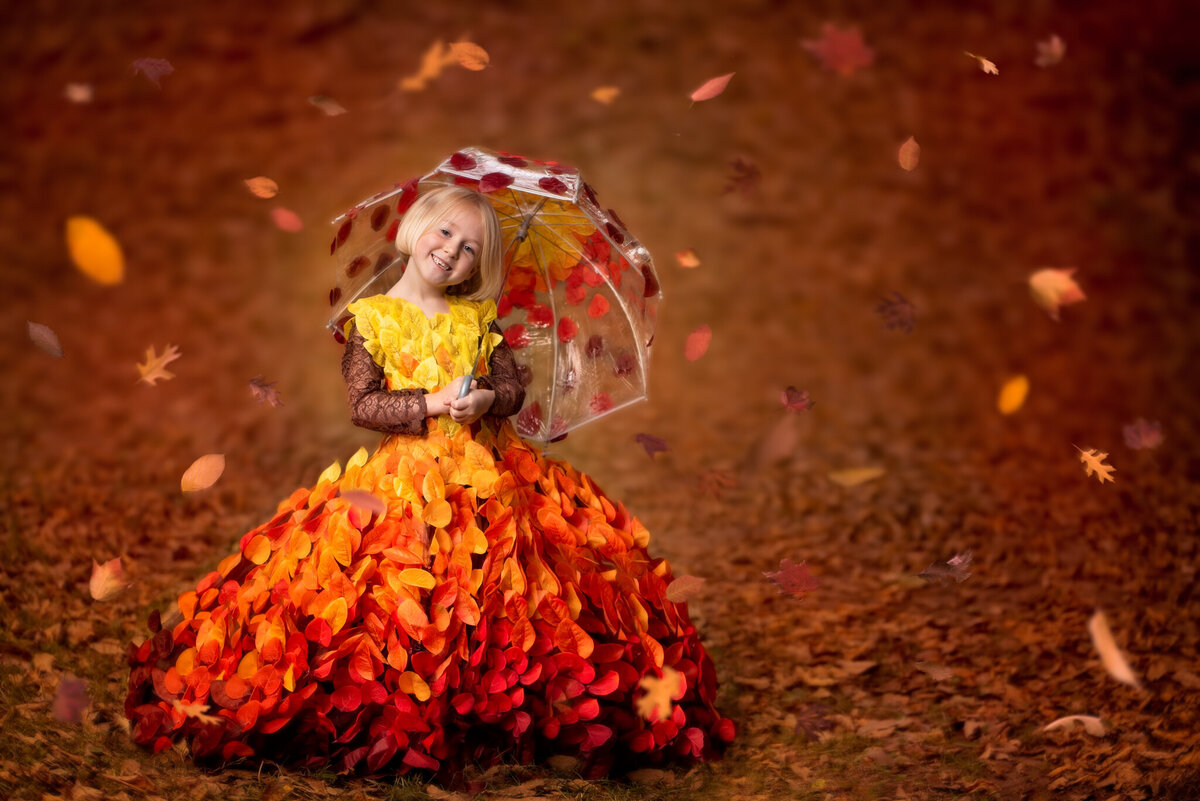 Enchanting portrait of a young girl wearing a stunning dress made of autumn leaves, twirling in a vibrant fall scene. Captured in Overland Park, Kansas, this whimsical setup is ideal for families seeking seasonal and artistic child photography.