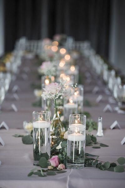 A long reception table scape with dozens of lit candles and greenery down the middle.