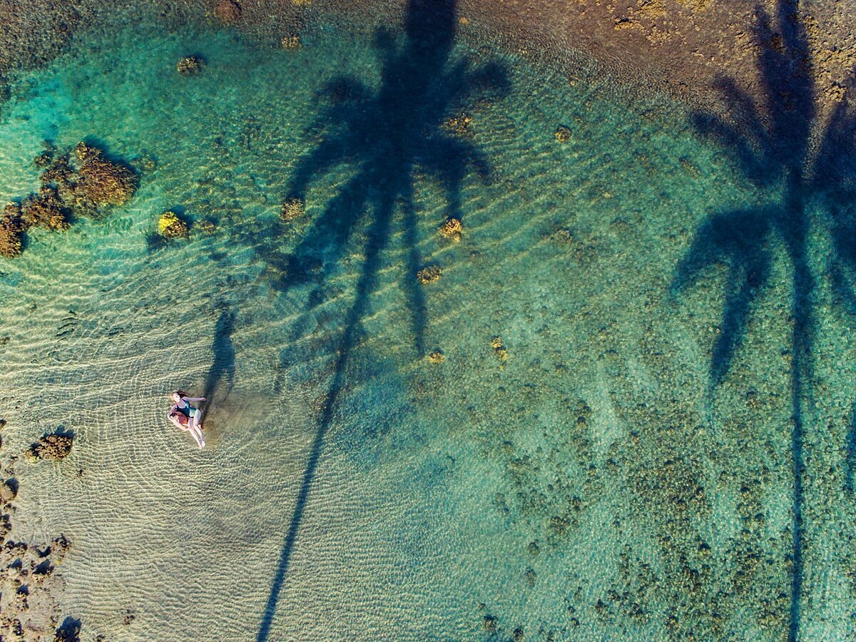 Drone photography of a couple in Wailea featuring palm tree shadows and rippling water off a shallow reef