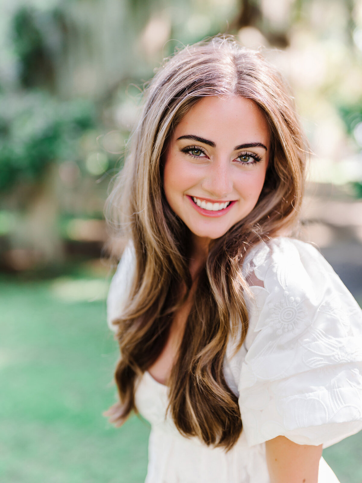 Beautiful senior girl in white top smiling with green Charleston background