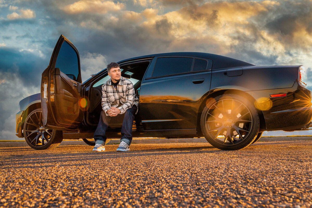 Senior boy posing with car in high school parking lot.