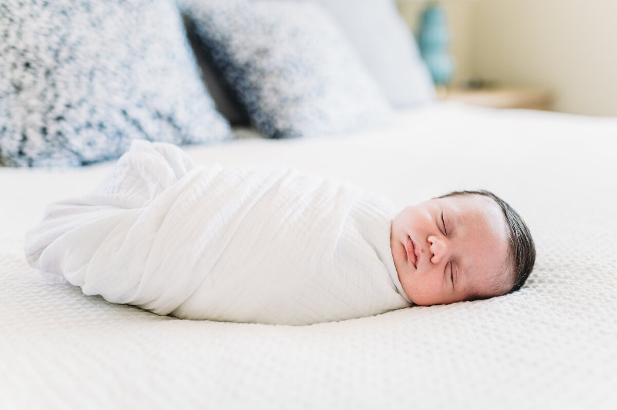 baby swaddled in white blanket lies on bed at home