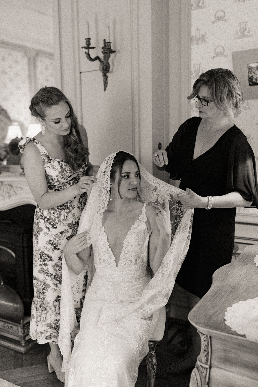 Mom and sister place an antique veil on the bride's head as she gets ready on her wedding day.