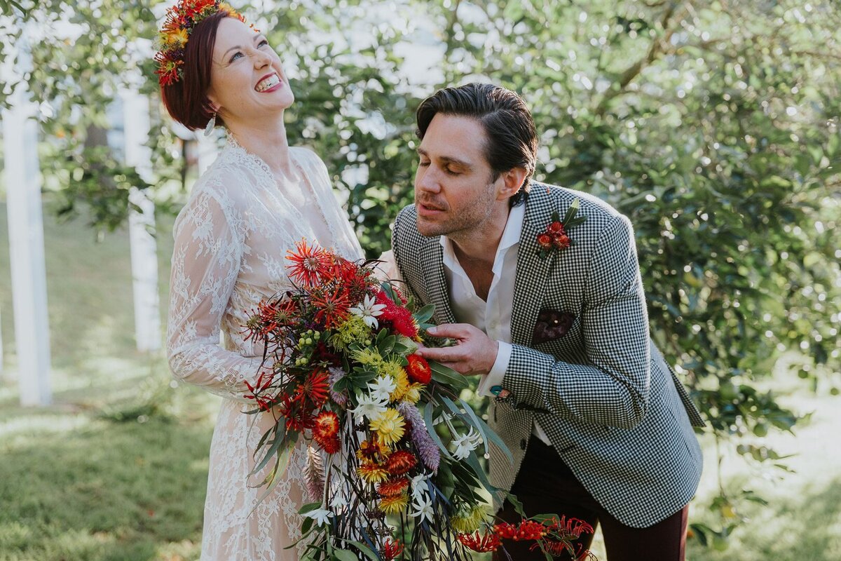 Happy, joyous and colourful photograph of a wedding couple. The bride is laughing while the groom smells the flowers in her bouquet. They look very classy and fun. Central Coast wedding photography.