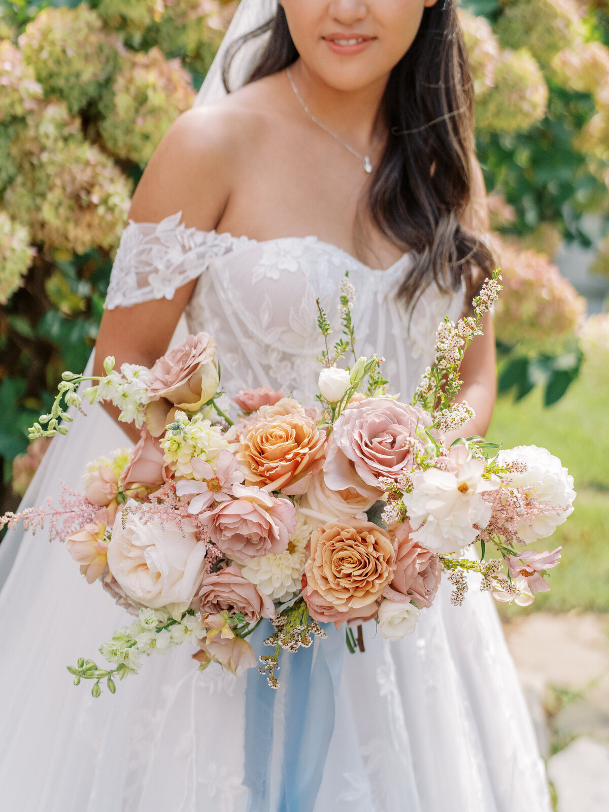 Bride holding a textured bouquet of neutral and blush roses with organic floral styling at Castle Ladyhawke.