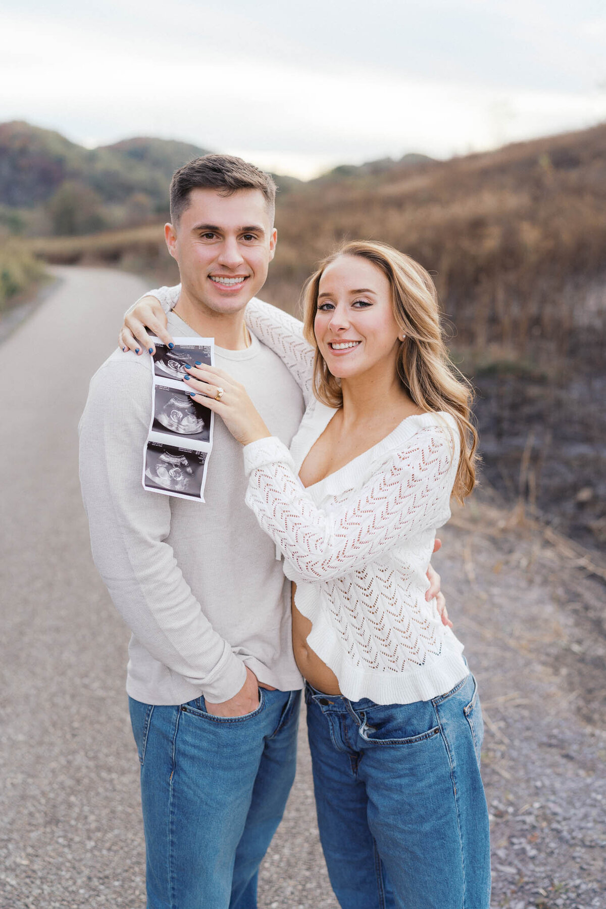 pregnant mom hugs husband while holding ultrasound at seven islands bird park in kodak tennessee during golden hour
