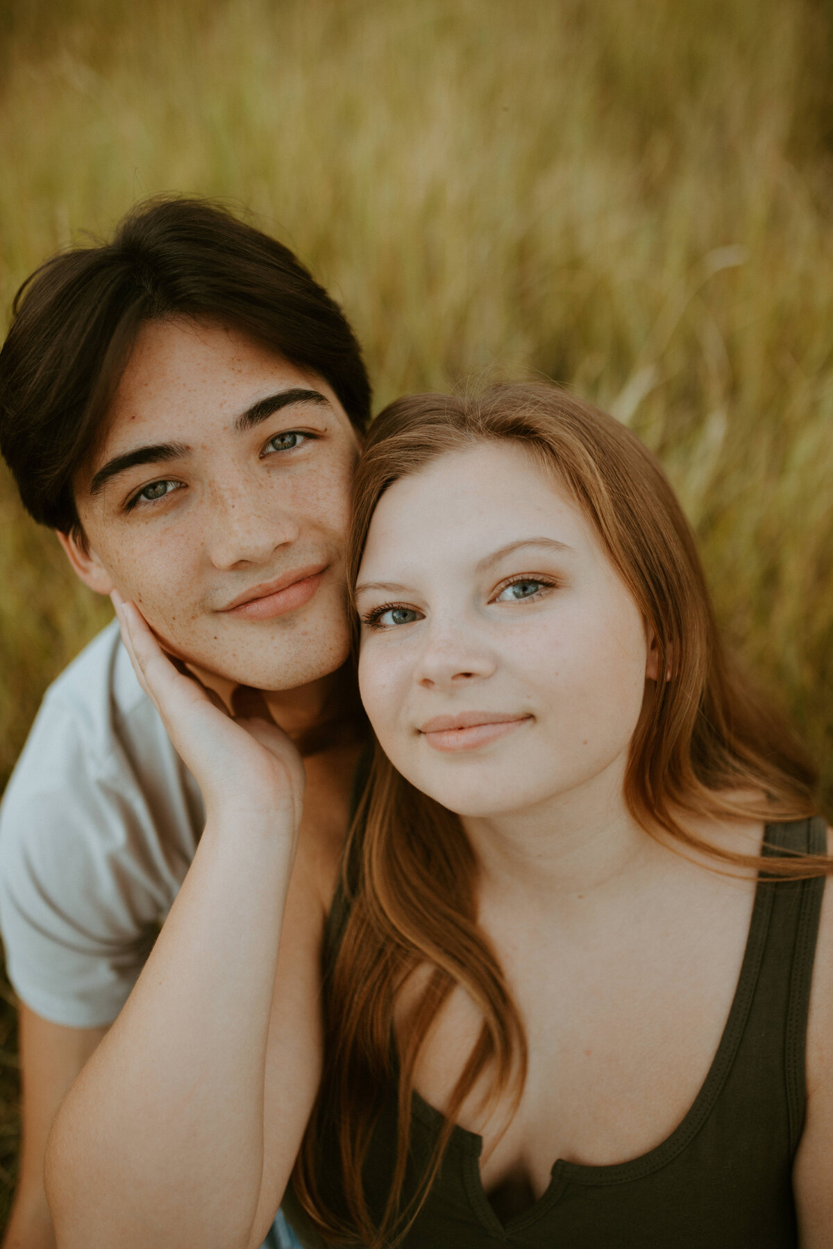 couples photos in field ,  both of them sitting close together looking at the camera