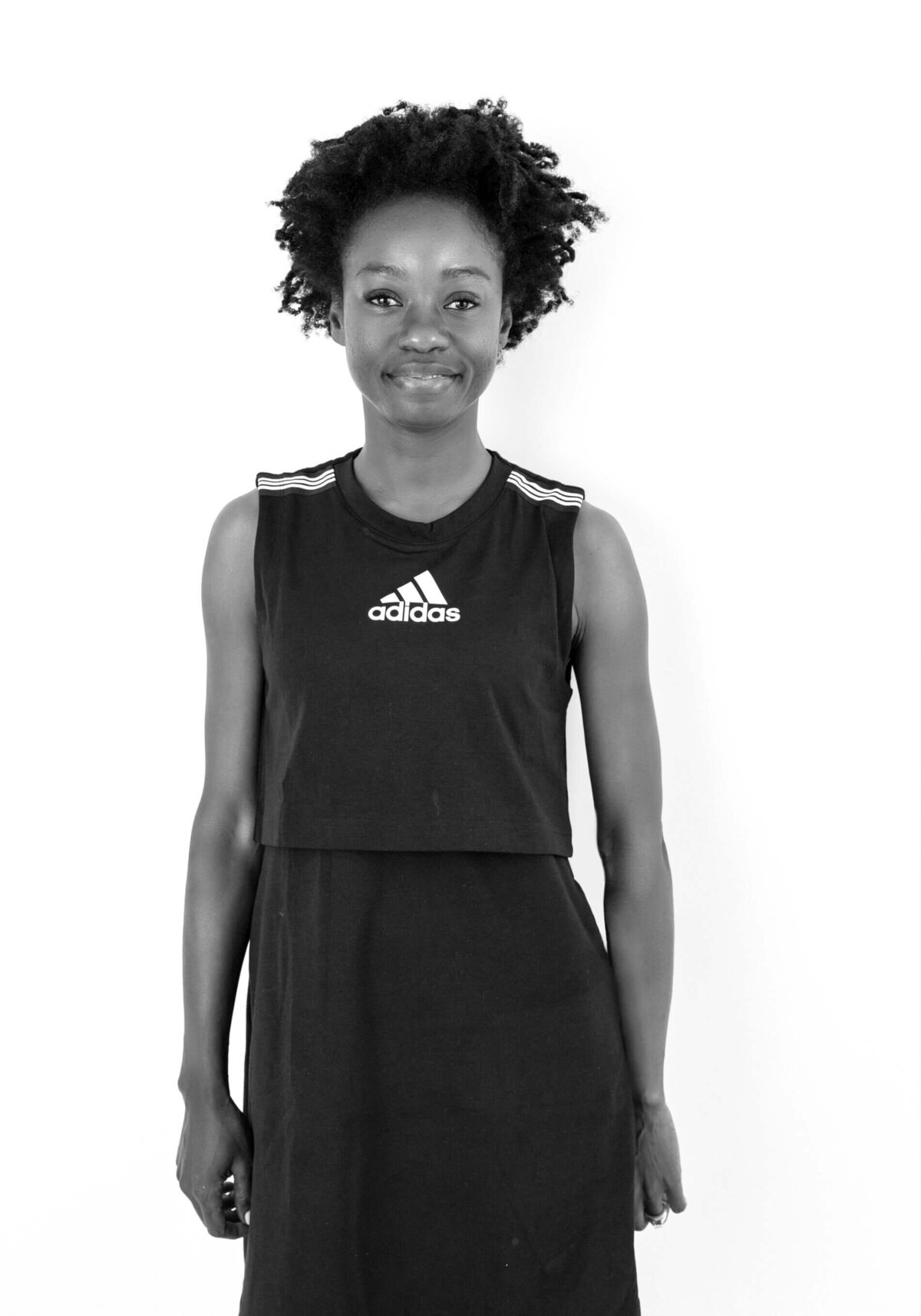 Black-and-white before shot of a woman in casual wear, smiling with hands relaxed at her sides.