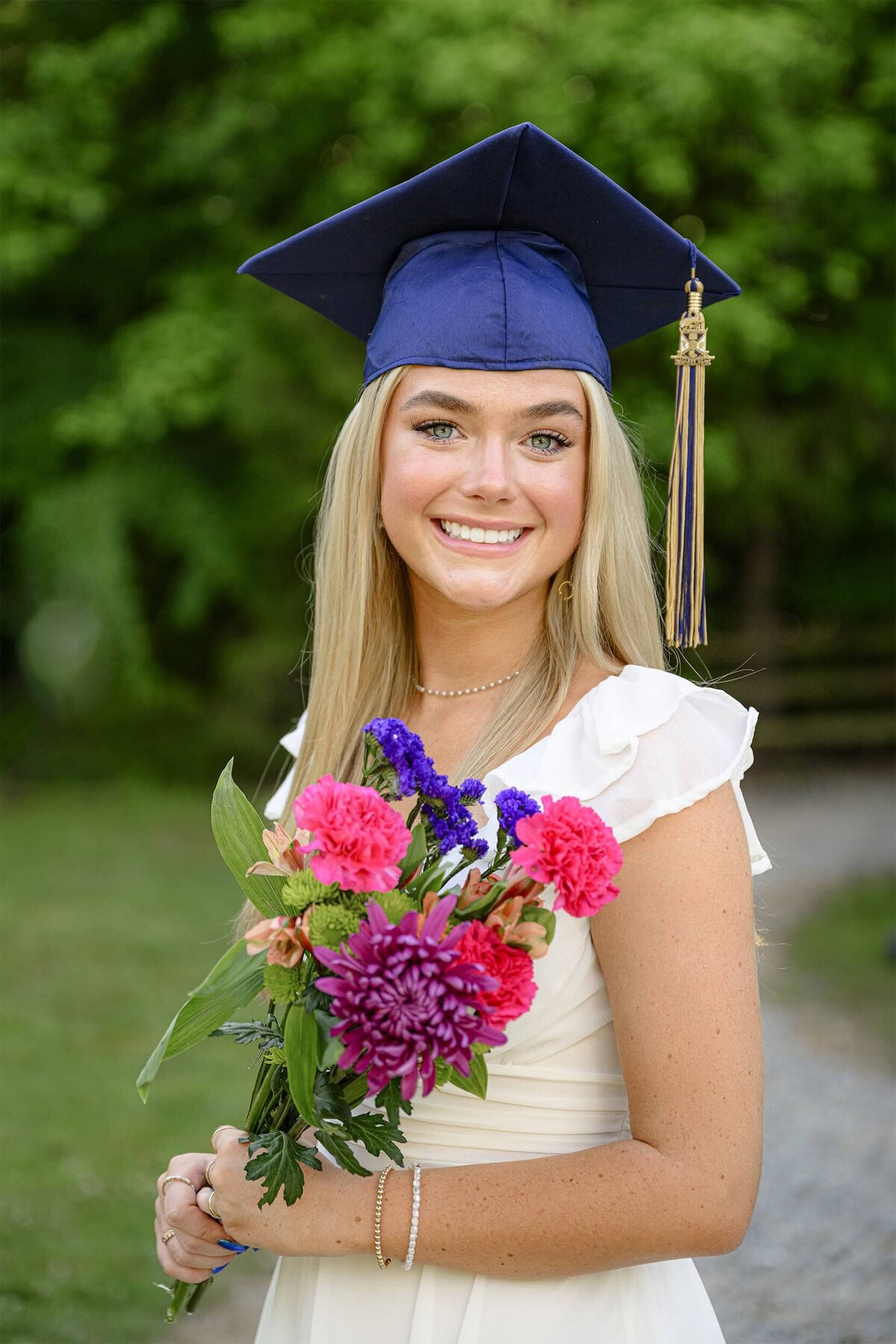 Cuthbertson High School Senior stands in her white dress and wearing her graduation cap and tassel holding a bouquet of flowers