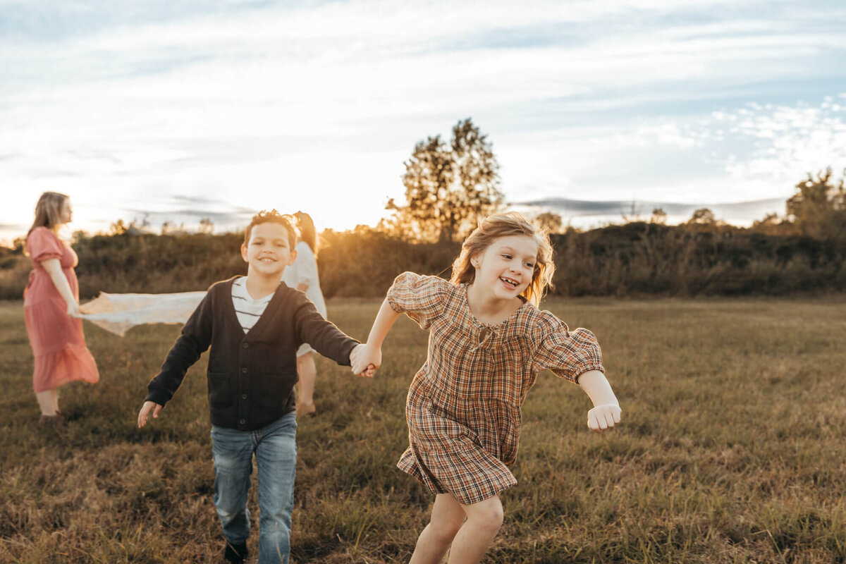 youngest daughter runs with brother under a lace blanket while holding his hand.