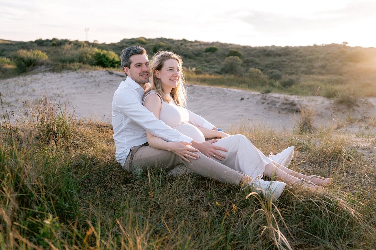 Man en vrouw zitten in de duinen terwijl ze lachend voor zich uit kijken