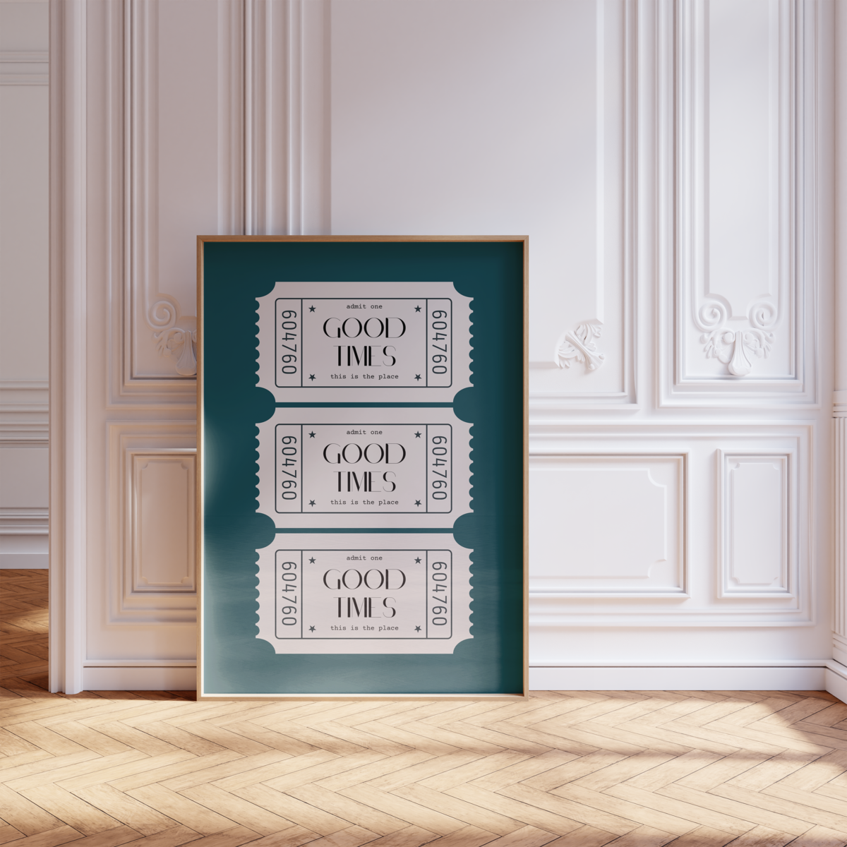 A framed poster by Sweet Pea Ink Creative featuring three vintage-style tickets with the text "GOOD TIMES" rests against an ornate white wall on a wooden herringbone floor.