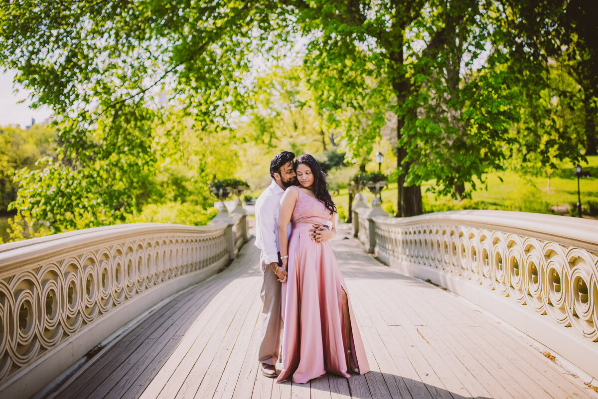 A couple in pink standing on the bow bridge in central park nyc