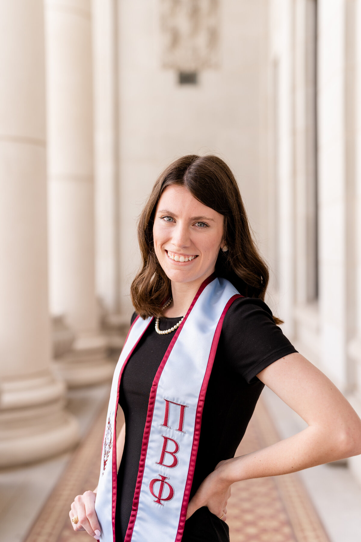 Texas A&M senior girl smiling with hand on hip wearing Pi Phi stole and black dress in the columns of the Administration Building