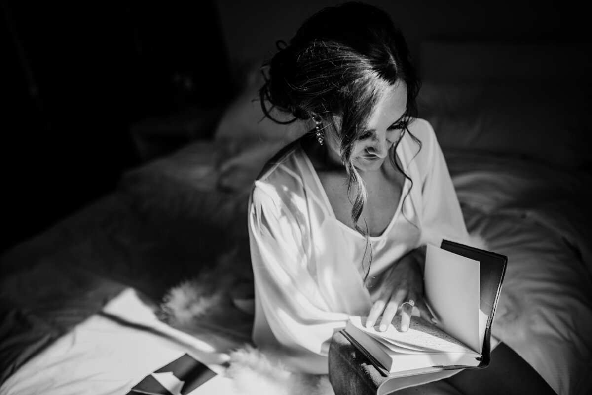 Baltimore wedding photographers captures bride the morning of her wedding in her bridal suite reading a journal note from her groom while sitting on the edge of her bed