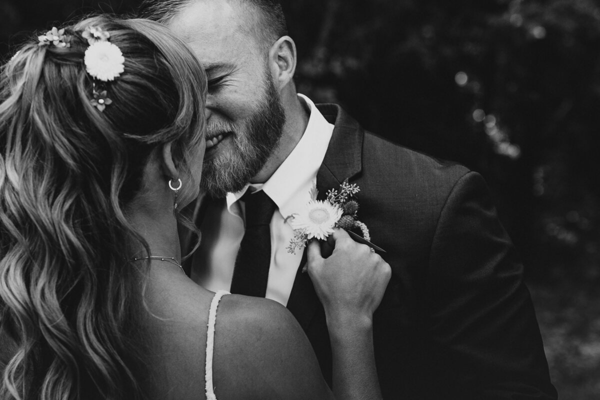 Intimate moment between a bride and groom in a black and white photo, with the bride affectionately adjusting the groom's boutonniere