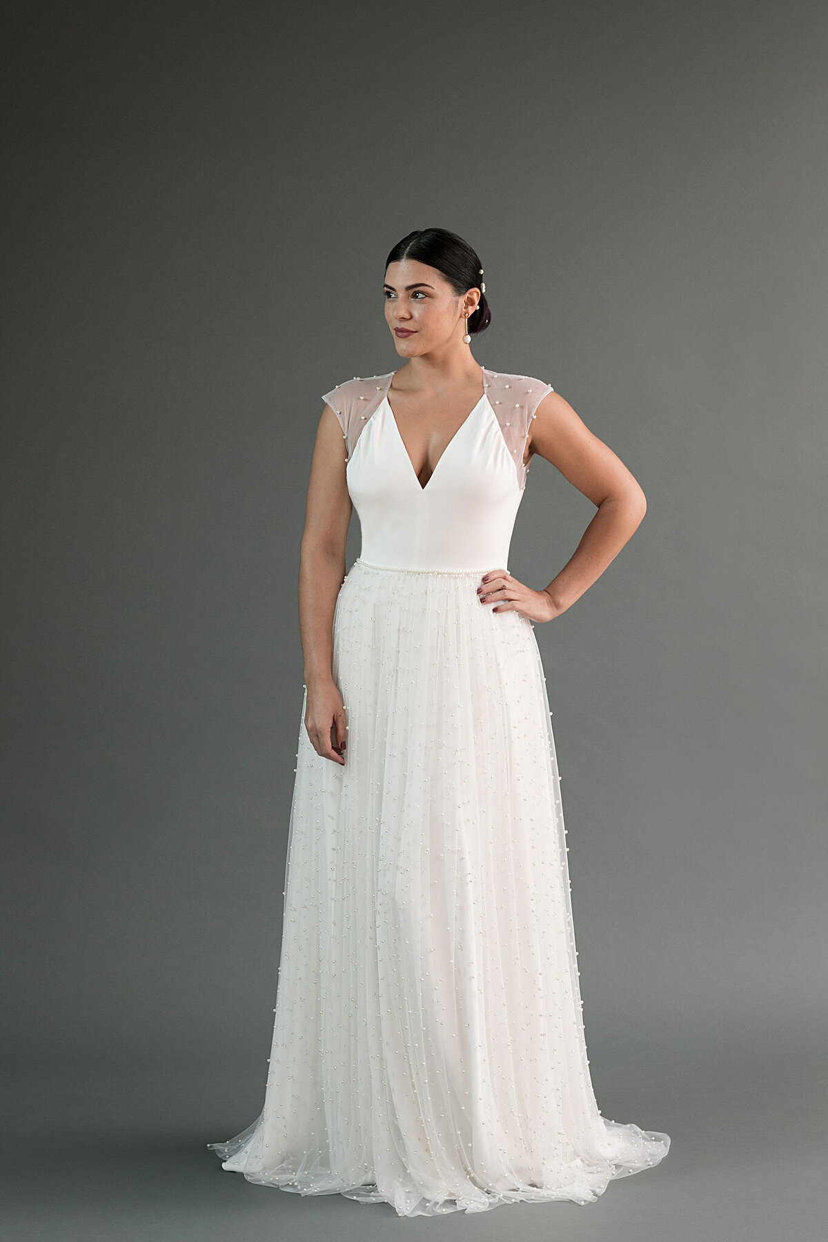 The Chika wedding dress style features a crepe v-neck top with an a-line skirt. The skirt has a gathered pearl net layer.