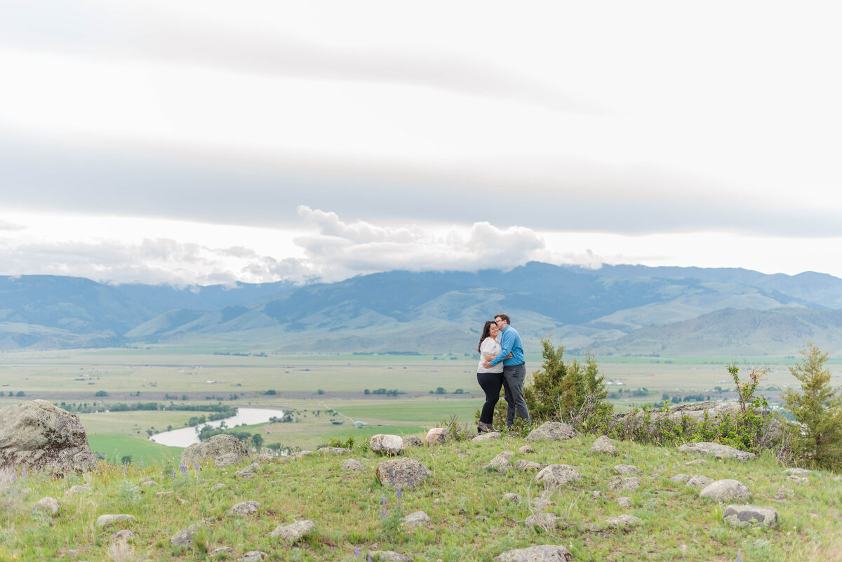 An engaged couple embraces in front of a mountain view by Laramee Love Photography